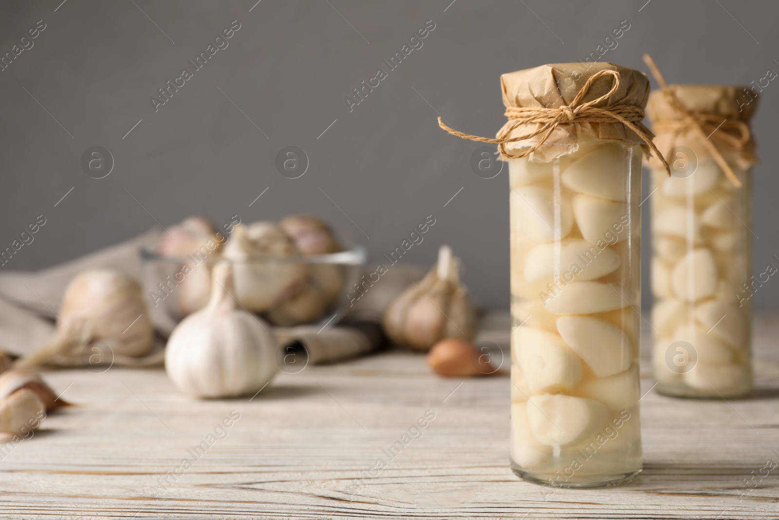 Photo of Preserved garlic in glass jar on wooden table. Space for text