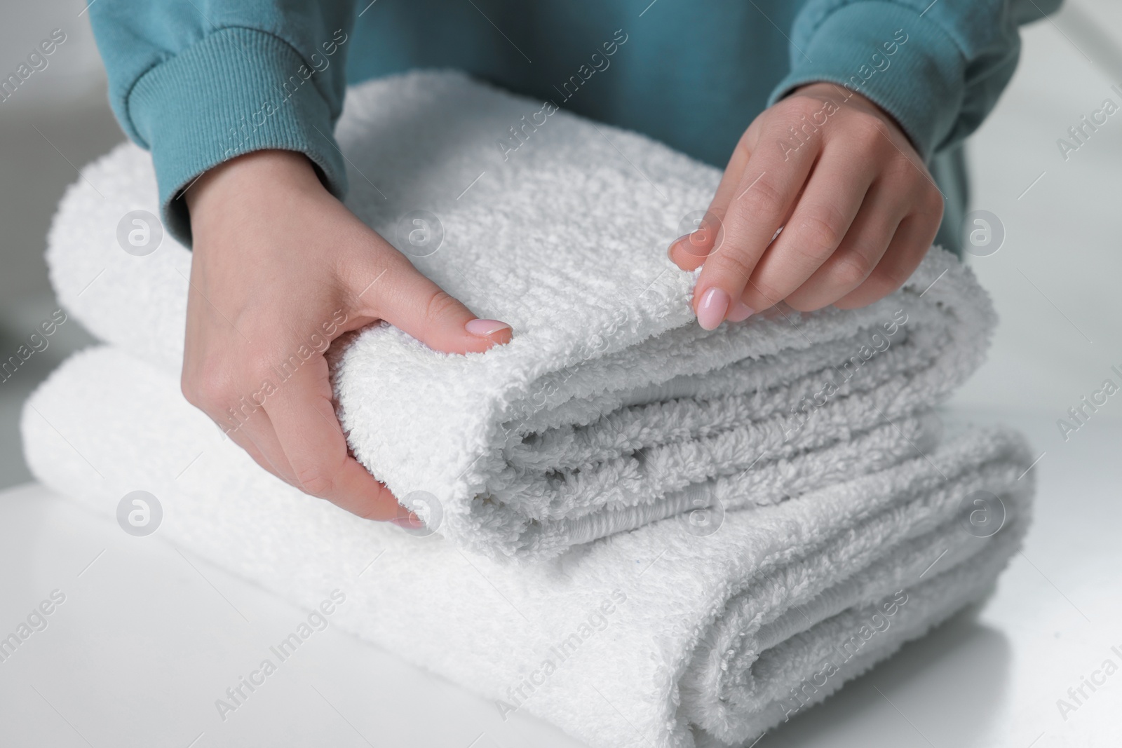 Photo of Woman touching soft white towel indoors, closeup