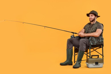 Photo of Fisherman with rod and tackle box on chair against yellow background