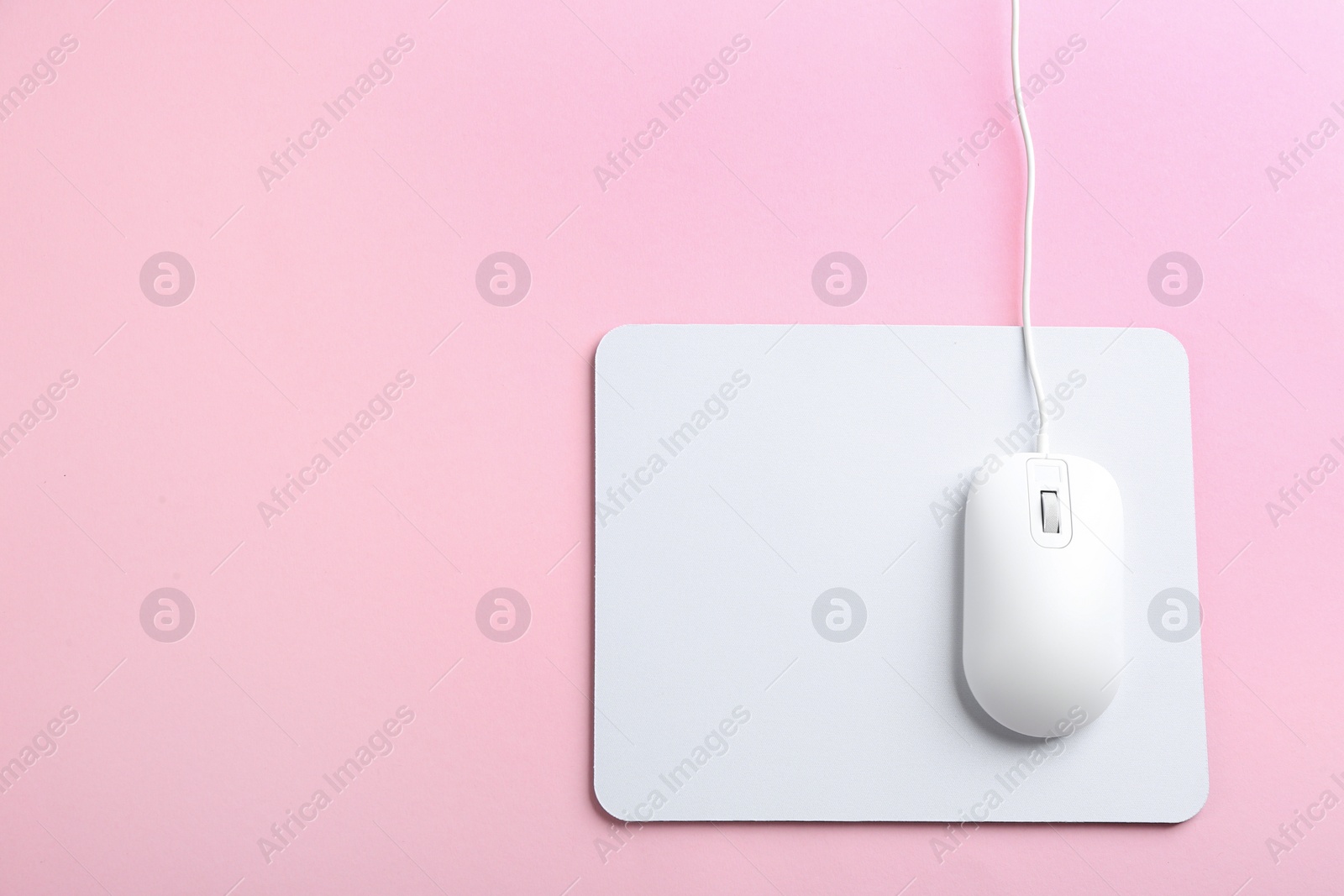 Photo of Modern optical wired mouse and white pad on pink background, top view. Space for text