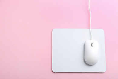 Photo of Modern optical wired mouse and white pad on pink background, top view. Space for text