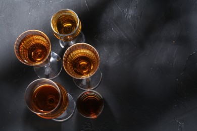 Photo of Many different liqueurs in glasses on dark textured table, flat lay. Space for text