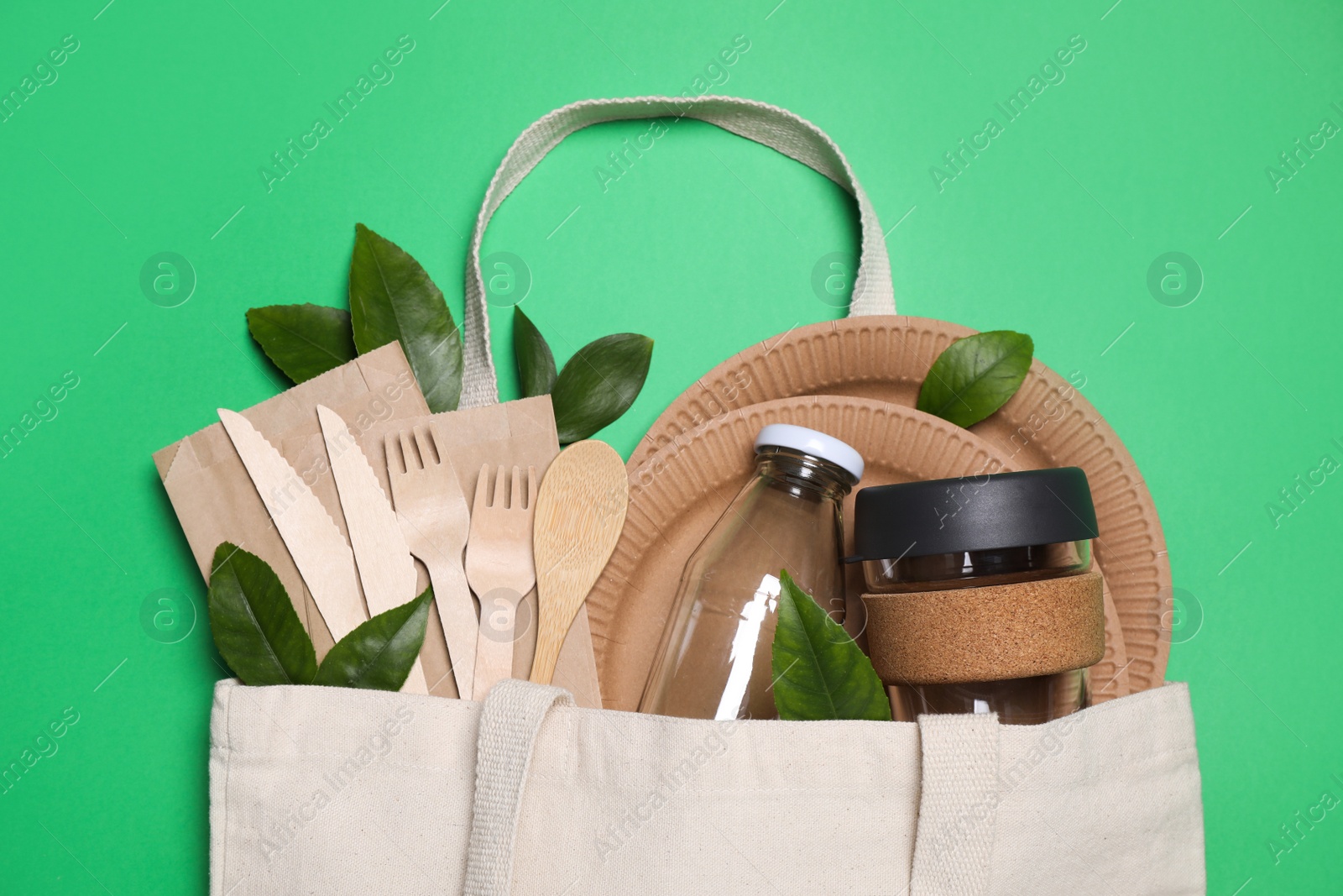 Photo of Flat lay composition with eco friendly dishware in bag on green background, top view