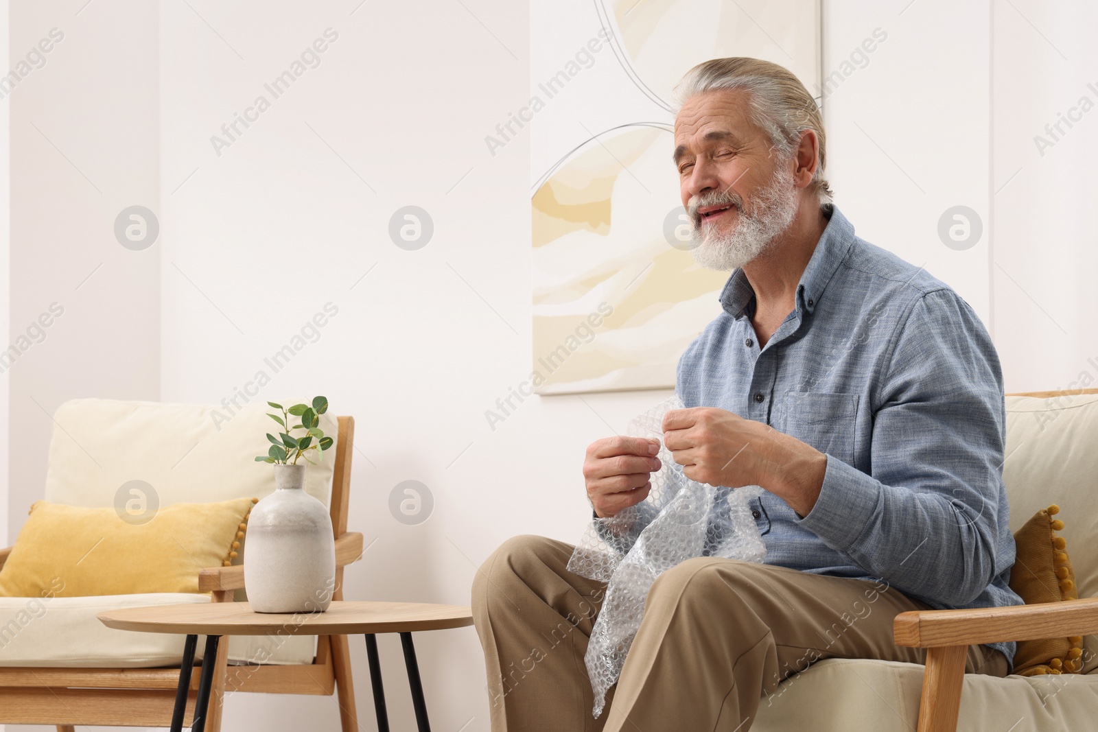 Photo of Senior man popping bubble wrap at home. Stress relief