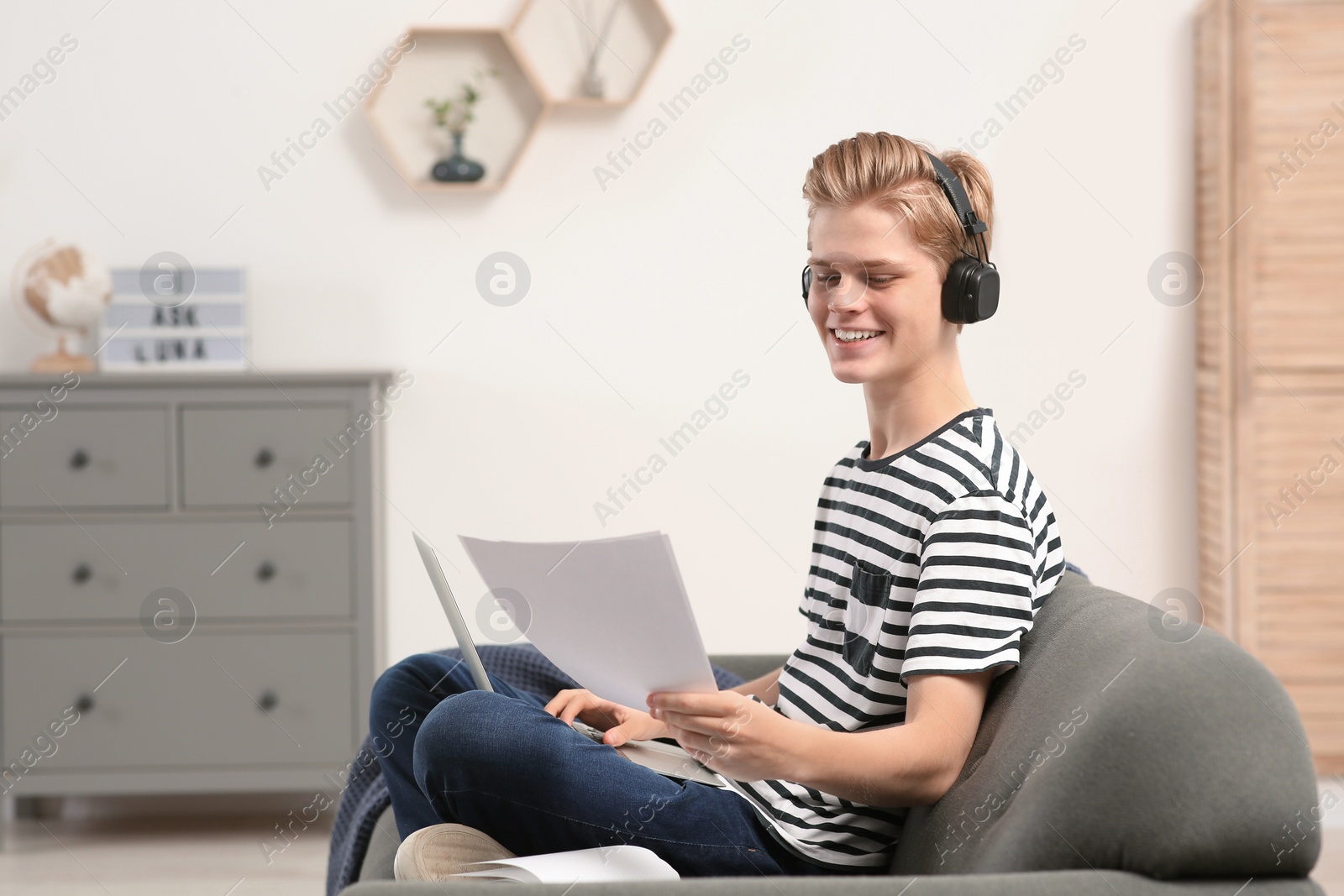 Photo of Online learning. Smiling teenage boy with laptop looking on essay at home