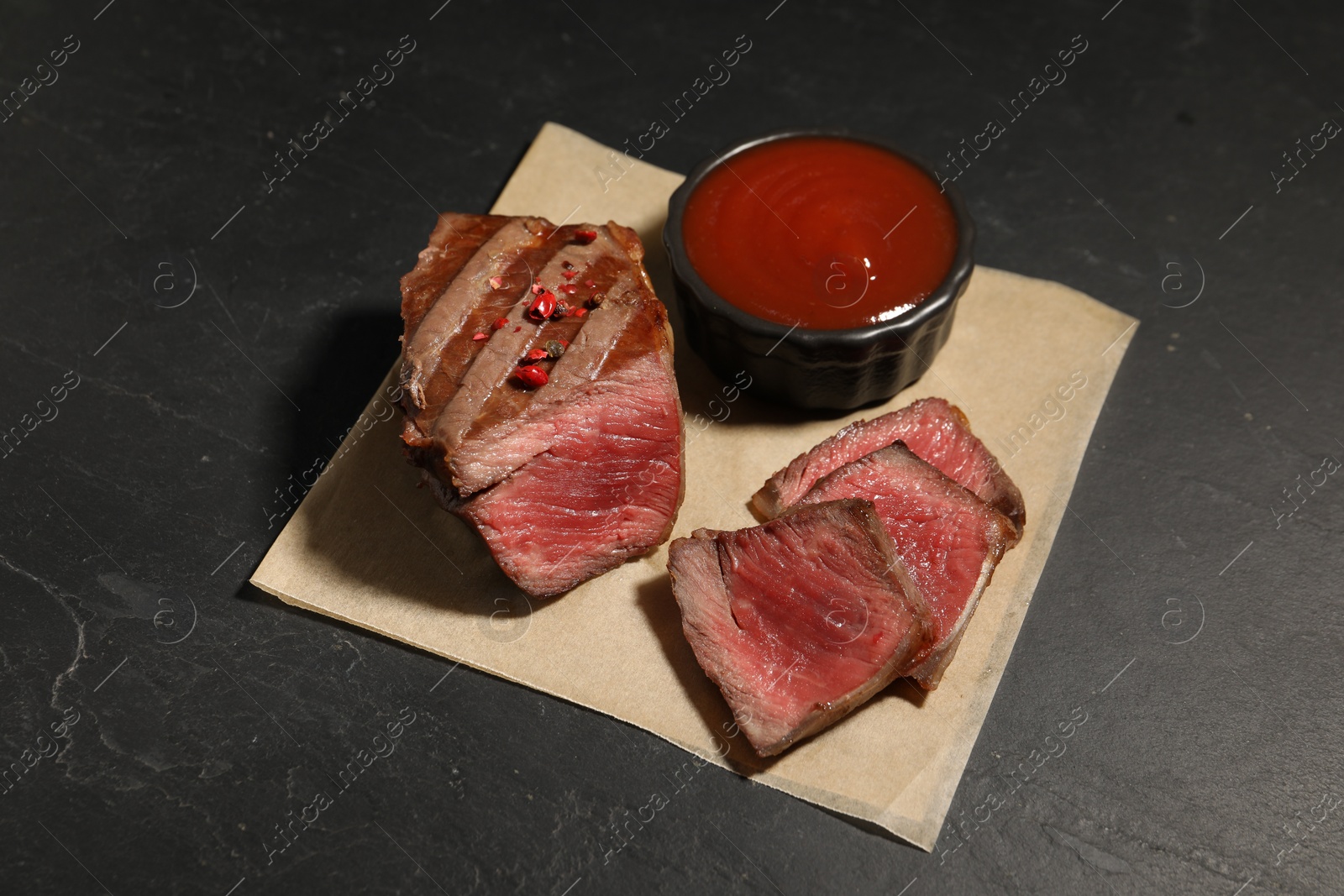 Photo of Delicious grilled beef steak with spices and tomato sauce on dark gray table