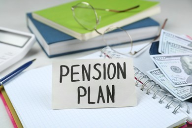 Photo of Card with phrase Pension Plan, notebook and dollar banknotes on office table, closeup