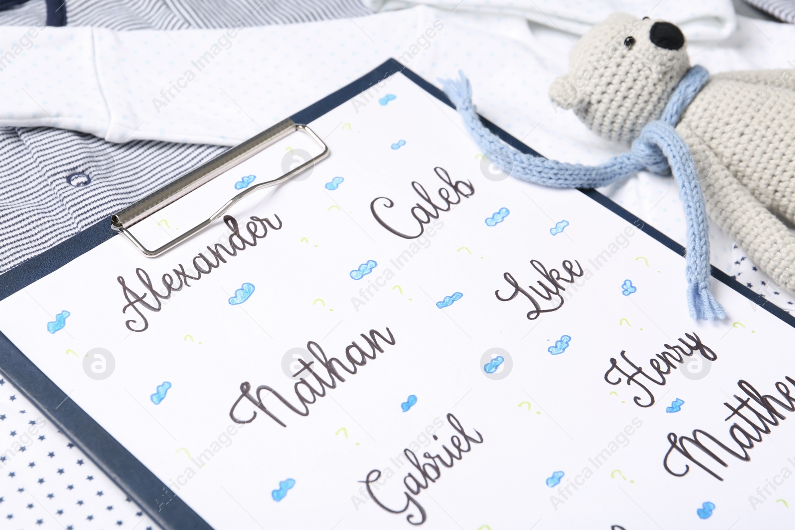 Photo of Clipboard with different baby names and toy on child's clothes, closeup