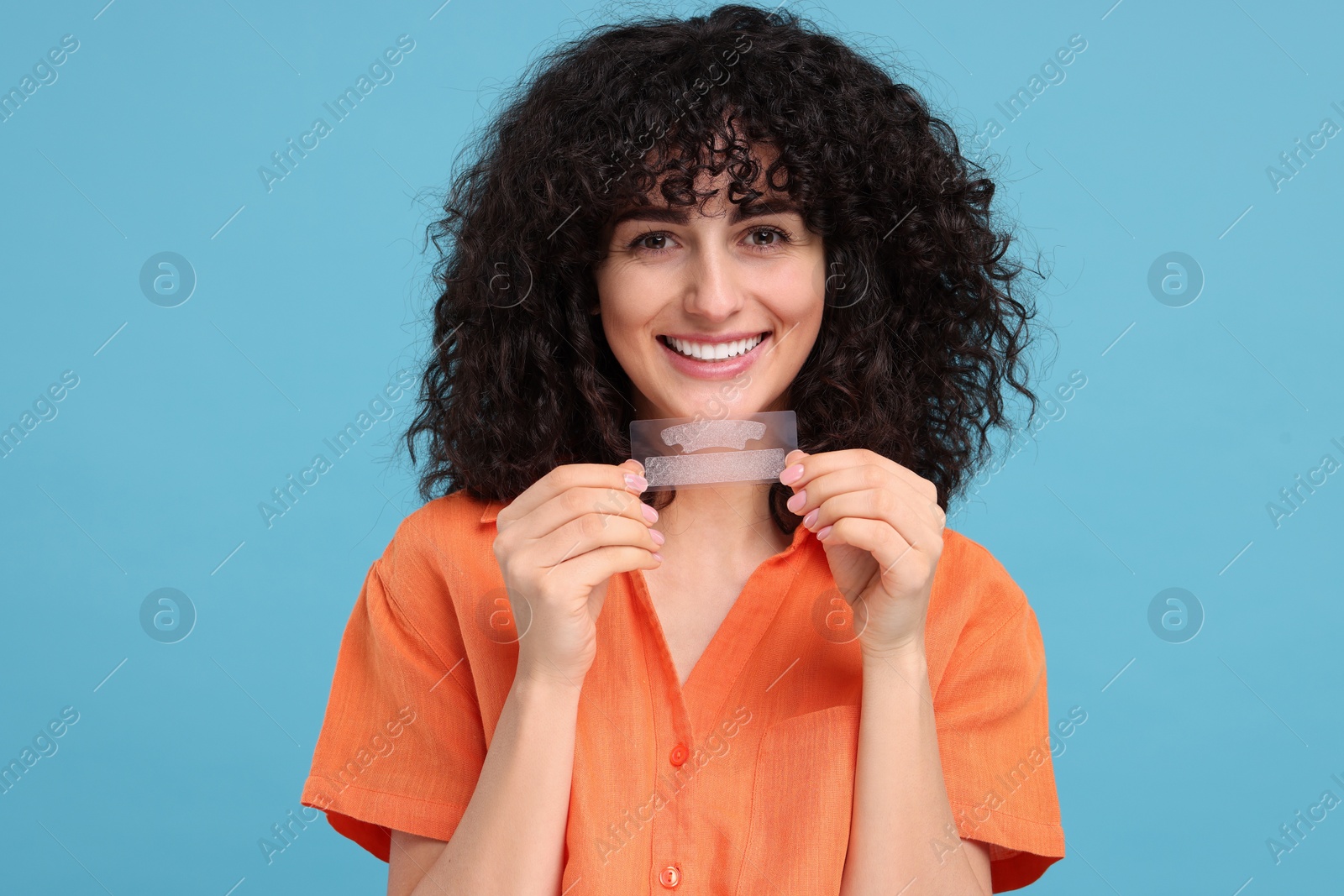 Photo of Young woman holding teeth whitening strips on light blue background