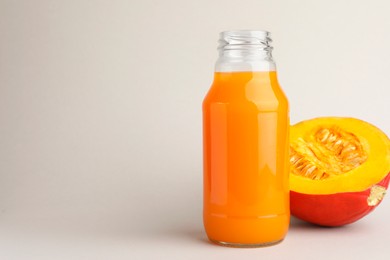 Photo of Tasty pumpkin juice in glass bottle and cut pumpkin on light background. Space for text