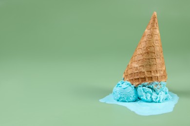 Photo of Melted ice cream and wafer cone on green background, space for text