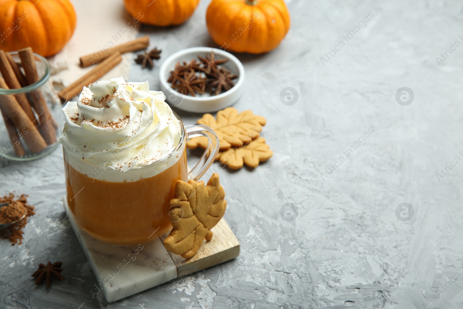 Photo of Cup of pumpkin spice latte with whipped cream, cookies and ingredients on light grey table. Space for text