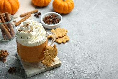 Photo of Cup of pumpkin spice latte with whipped cream, cookies and ingredients on light grey table. Space for text