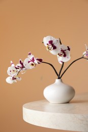 Vase with orchid flowers on white table near light brown wall