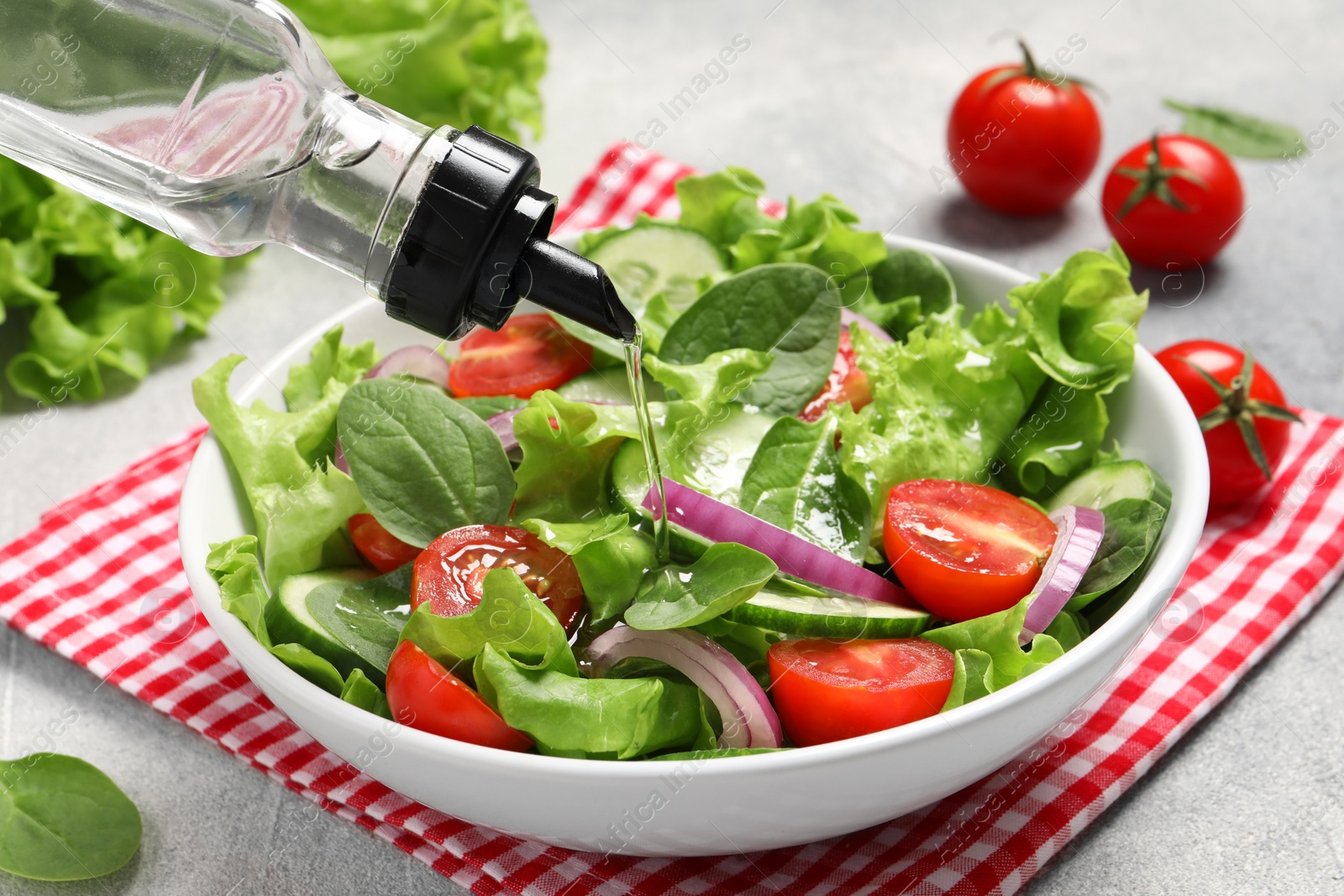 Photo of Pouring oil into delicious vegetable salad on light grey table, closeup