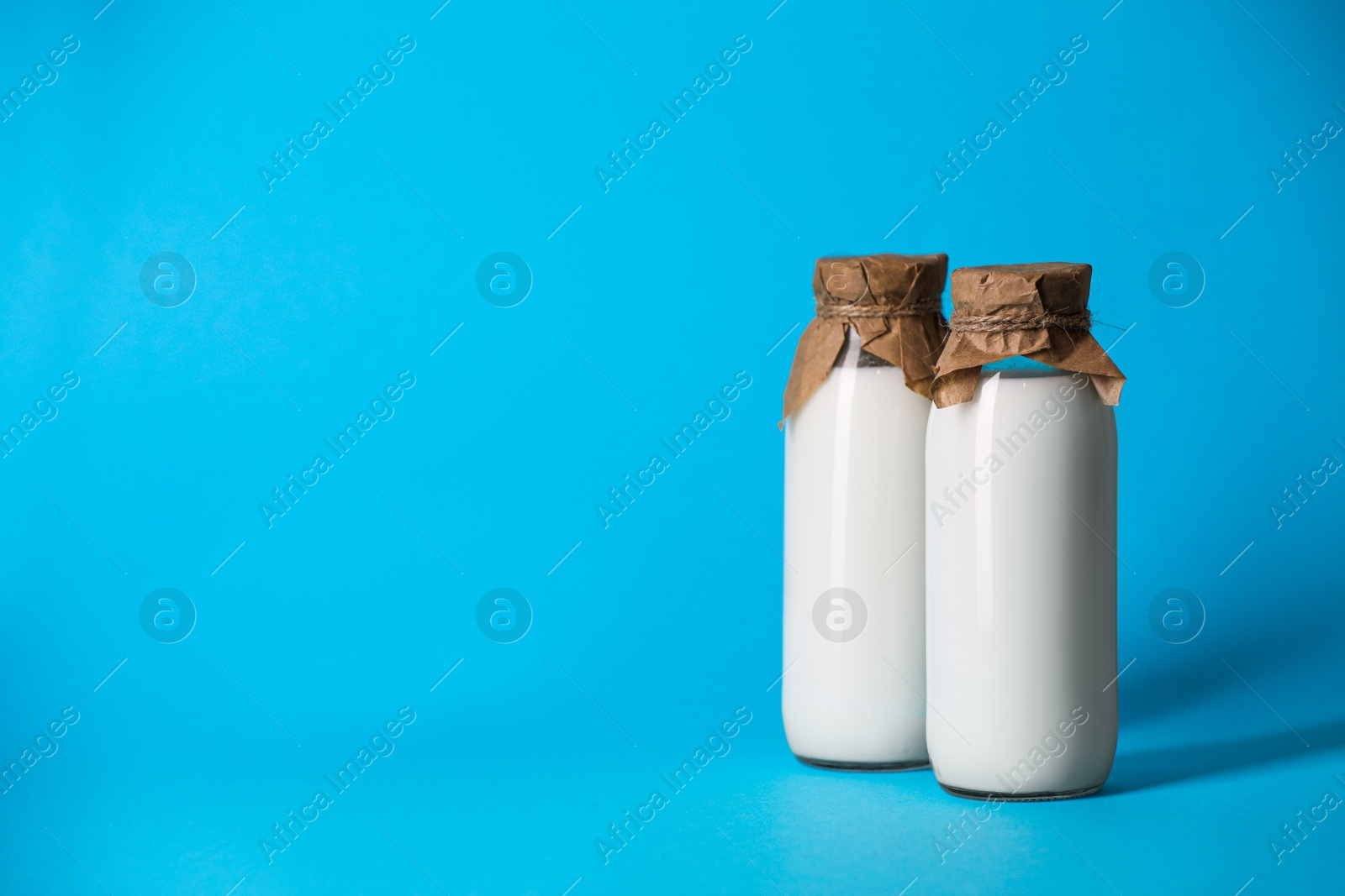 Photo of Tasty fresh milk in bottles on light blue background, space for text