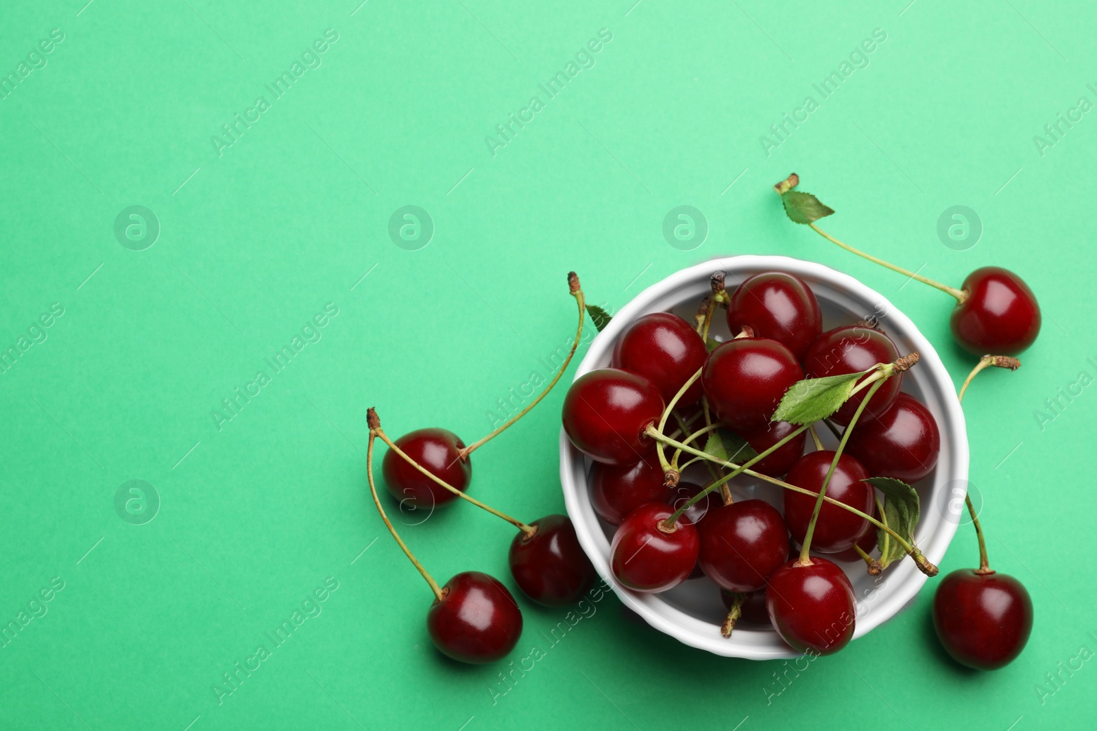 Photo of Bowl of tasty ripe cherries on green background, flat lay with space for text