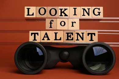 Photo of Staff recruitment concept. Phrase Looking For Talent made of wooden cubes and binoculars on orange background
