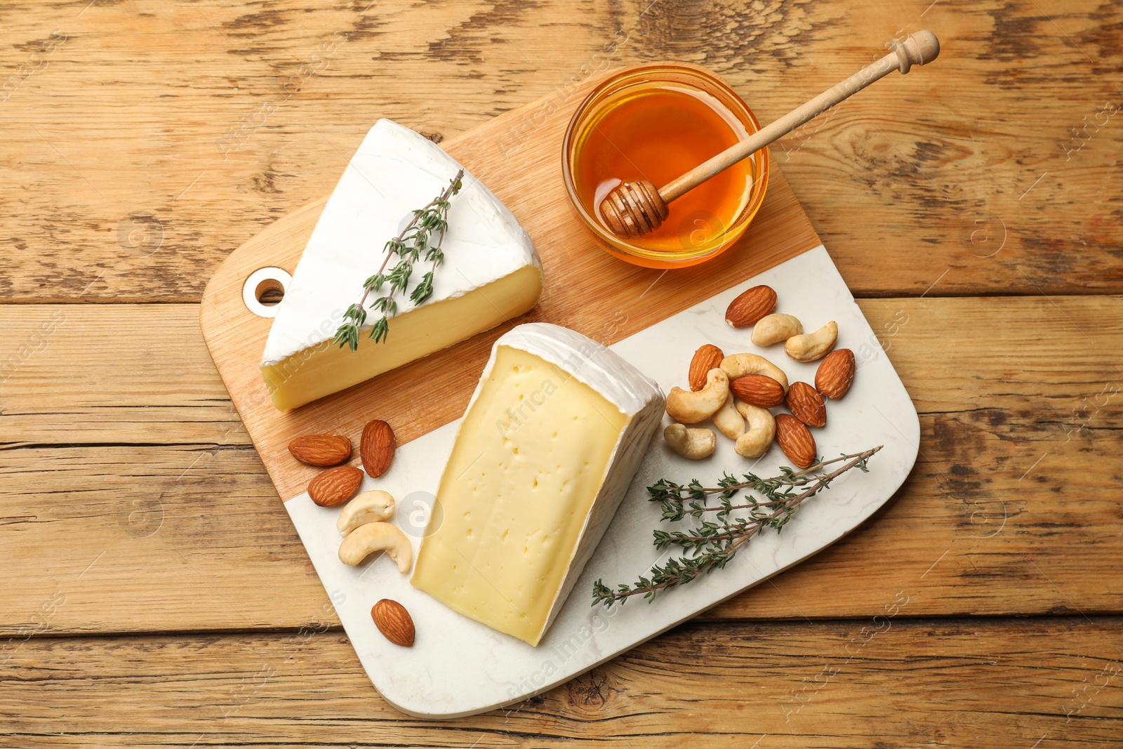 Photo of Tasty Camembert cheese with thyme, honey and nuts on wooden table, top view