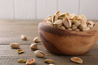 Tasty pistachios in bowl on wooden table, closeup. Space for text