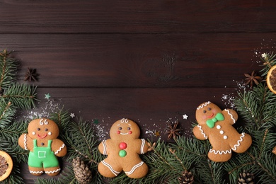 Decorated Christmas cookies and fir tree branches on wooden table, flat lay. Space for text