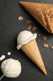 Ice cream scoops in wafer cones on dark gray textured table, flat lay