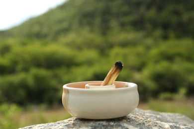 Photo of Burnt palo santo stick on stone surface outdoors, closeup