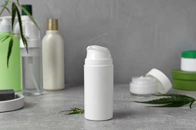 Photo of Hemp cosmetic products and green leaves on grey table