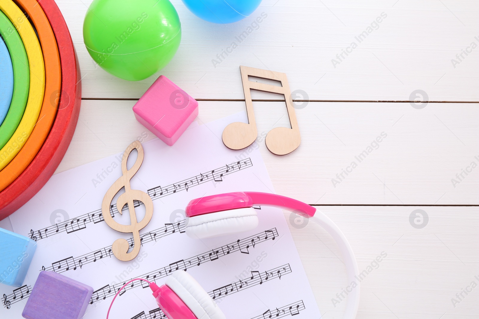 Photo of Notes, music sheet, headphones and toys on white wooden table, flat lay with space for text. Baby song concept