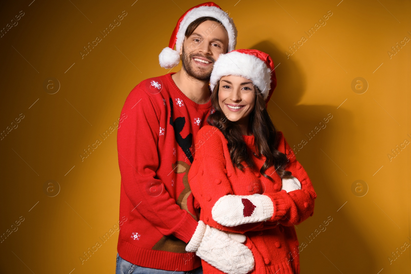 Photo of Young couple in Christmas sweaters and hats on yellow background