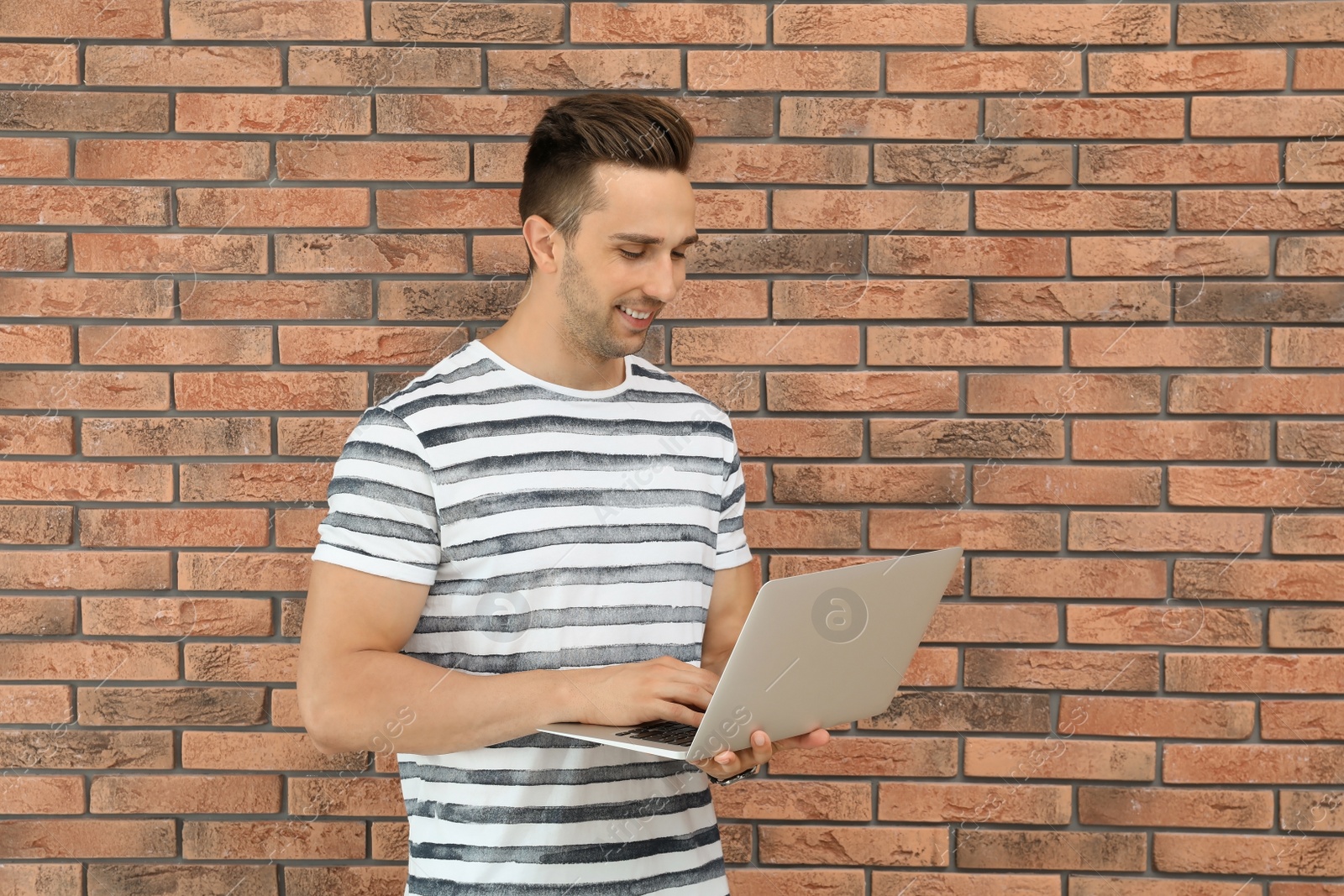 Photo of Man in casual clothes with laptop near brick wall