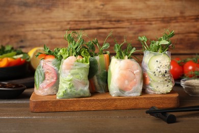 Photo of Many different delicious rolls wrapped in rice paper on wooden table