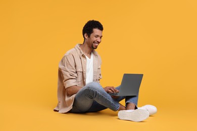 Happy man using laptop against orange background