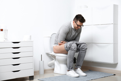 Photo of Man with stomach ache sitting on toilet bowl in bathroom