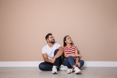 Young couple sitting on floor near beige wall indoors