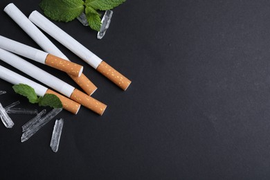 Photo of Cigarettes, menthol crystals and mint on black background, flat lay. Space for text