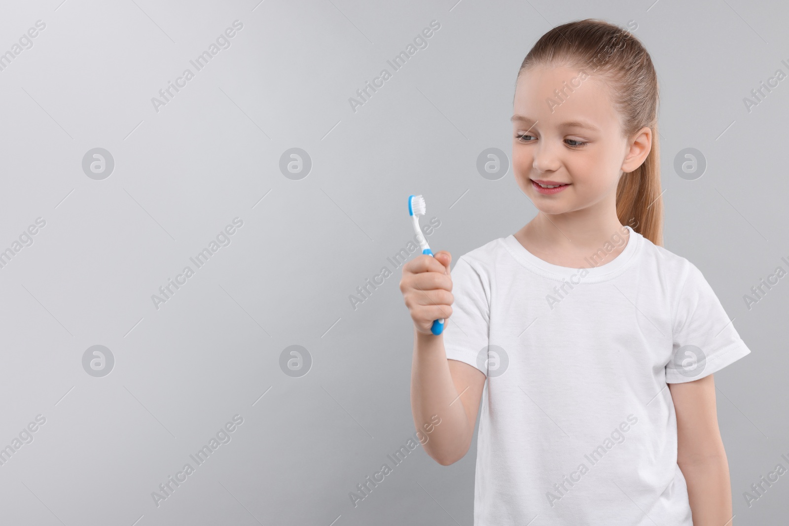 Photo of Happy girl holding toothbrush on light grey background. Space for text