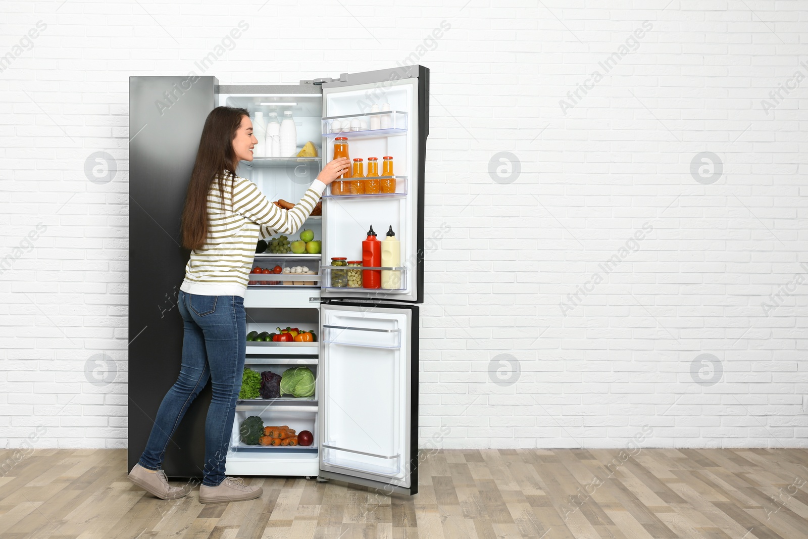 Photo of Young woman taking juice out of refrigerator indoors, space for text