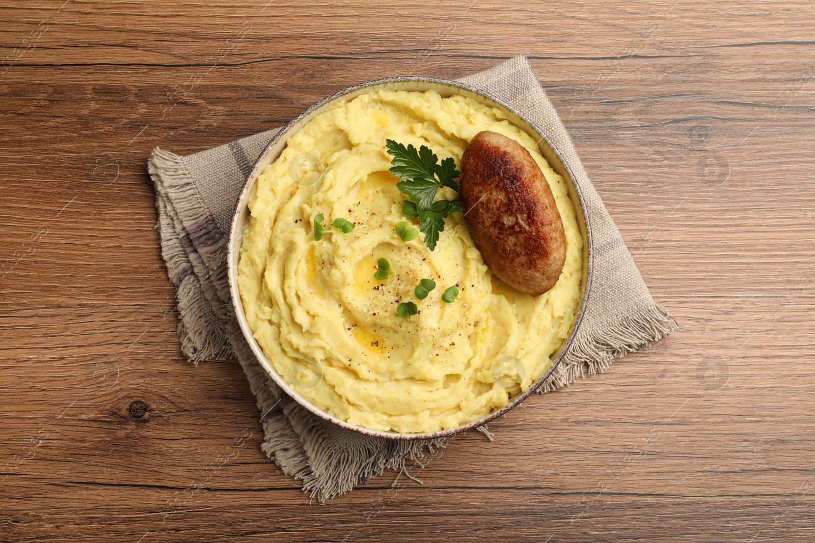 Photo of Bowl of tasty mashed potatoes with parsley, black pepper and cutlet served on wooden table, flat lay