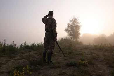 Photo of Man with hunting rifle wearing camouflage outdoors, back view. Space for text