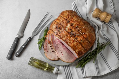 Photo of Delicious baked ham, carving fork, knife, oil and rosemary on light grey table, flat lay