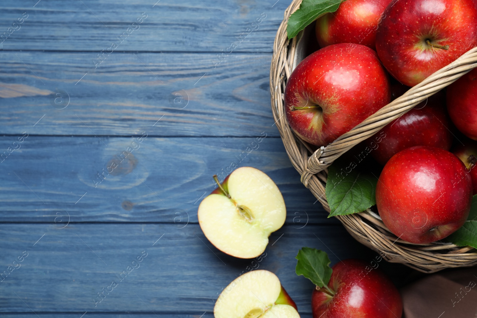Photo of Juicy red apples in wicker basket on blue wooden table, flat lay. Space for text