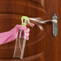 Woman sanitizing door handle with antiseptic spray, closeup. Be safety during coronavirus outbreak