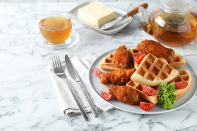 Photo of Tasty Belgian waffles served with fried chicken, tomatoes, lettuce and tea on white marble table. Space for text