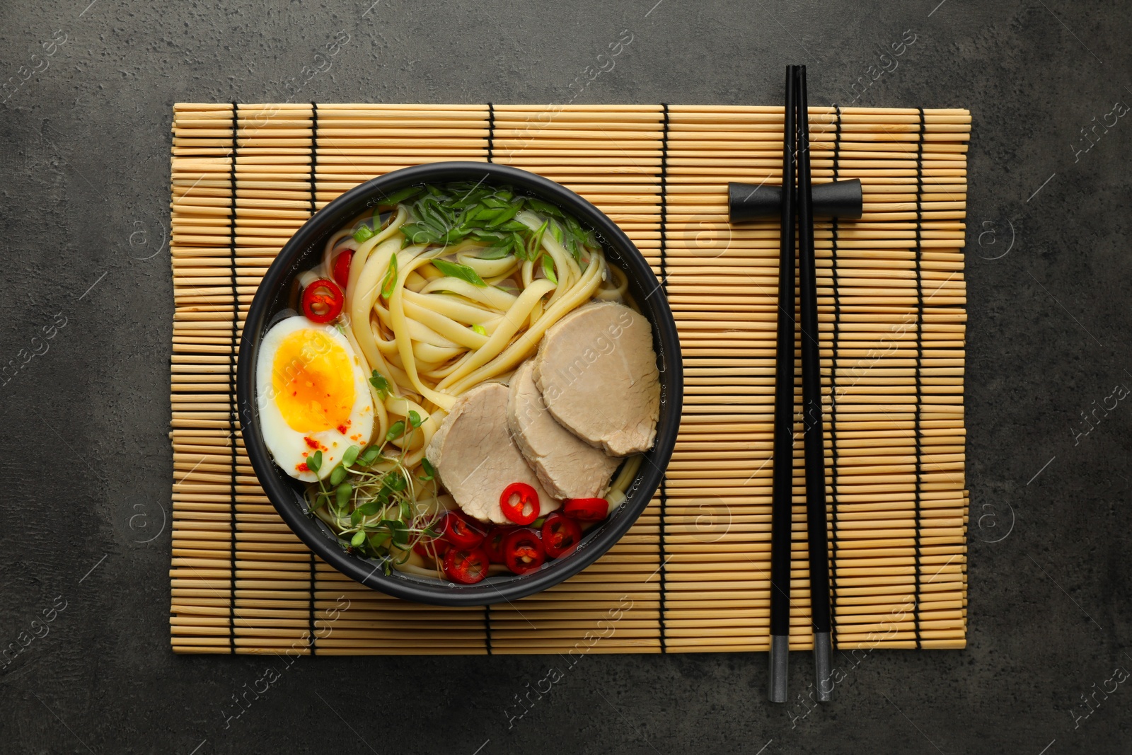 Photo of Delicious ramen with meat in bowl and chopsticks on grey textured table, top view. Noodle soup