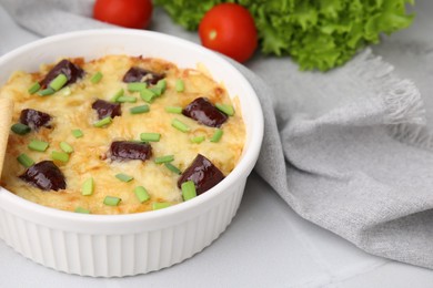 Photo of Tasty sausage casserole with green onions in baking dish served on white tiled table, closeup