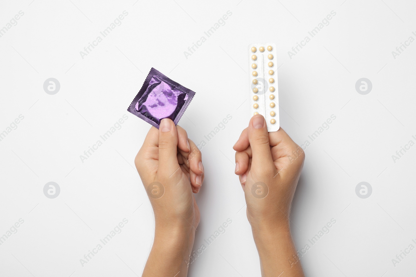 Photo of Woman holding condom and birth control pills on white background, top view. Safe sex