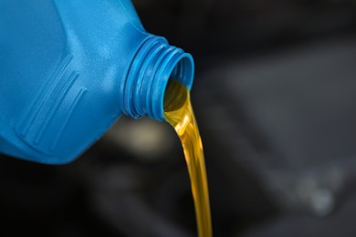 Photo of Pouring motor oil from blue container against blurred background, closeup. Space for text