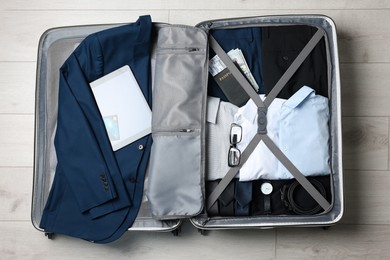 Folded clothes, money and accessories in open suitcase on wooden floor, top view. Business trip planning