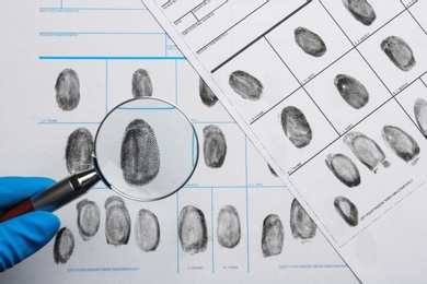 Photo of Criminalist studying fingerprints with magnifying glass, top view